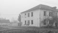 An abandoned two-story wooden house by the road on a foggy day, black and white photo Royalty Free Stock Photo