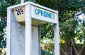 Abandoned vandalized phone booth among trees and weeds