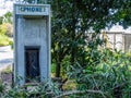 Abandoned vandalized phone booth among trees and weeds