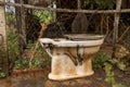 Abandoned Vintage Old Toilet Outside Messy Storehouse - Wet Concrete Ground/ Wire Fence with Wood Pole/ Water PVC Pipes - Side Vi Royalty Free Stock Photo