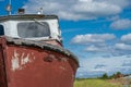 An abandoned and weathered red rusty boat sits in a marshy grass in Homer Alaska