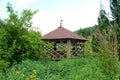 Abandoned wooden well with decorated walls and roof surrounded with overgrown vegetation Royalty Free Stock Photo