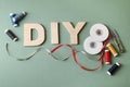 Abbreviation DIY made of wooden letters and sewing supplies on olive background, flat lay