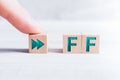 The Abbreviation FF Formed By Wooden Blocks And Arranged By A Male Finger On A White Table