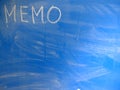 Abbreviation MEMO written on a blue, relatively dirty chalkboard by chalk. Located in the upper left corner of the image making