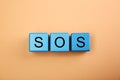 Abbreviation SOS (Save Our Souls) made of light blue cubes with letters on pale coral background, top view Royalty Free Stock Photo