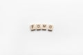 Abbreviation word FOMO from wooden blocks on white background. FOMO means Fear Of Missing Out, non-stop internet surfing. Concept