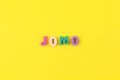 Abbreviation word JOMO in multicolored wooden letters on pastel yellow background. JOMO - Joy Of Missing Out. Opposition, choice,