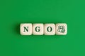 The abbreviation word NGO nongovernmental organization written on wooden cubes with people icon on green background