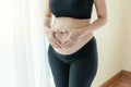 Abdomen pregnant young woman use her hands making symbol heart beside windows in the bedroom. Body pregnancy mother