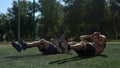 Abdominal exercises. Two topless sportsman doing sit-ups in unison on the grass.