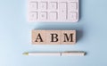 ABM word on wooden block with pen and calculator on blue background