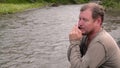 Aboriginal sitting on a river bank and plays a jews-harpon