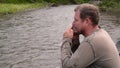 Aboriginal sitting on a river bank and plays a jews-harpon