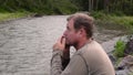 Aboriginal sitting on a river bank and plays a jews-harpon