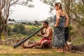 Aboriginal woman looks at man blowing black didgeridoo in Newcastle, Australia