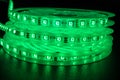 From above bobbins with three roll of glowing LED strip lighting,colour green, placed on table in dim room