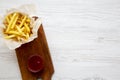 From above french fries with ketchup on wooden board. White wooden background.