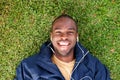 Above of happy black man lying on grass listening to music with earphones