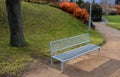 Above the ornamental pond in the park are several gray metal transparent benches on the park gravel sidewalk. autumn leaves lying