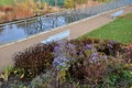 Above the ornamental pond in the park are several gray metal transparent benches on the park gravel sidewalk. autumn leaves lying