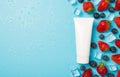 Above photo of berries strawberries blueberries transparent cubes ice water drops and white tube of cream isolated on the blue