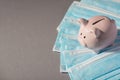Above photo of moneybox pink pig with pile of blue masks isolated on the grey background