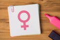 Above photo of notes sticker with image of female gender symbol paperclips and pink marker isolated on the wooden backdrop