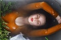 Portrait of young adult woman lying in bathtub filled with charcoal water