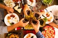 Above and top view in a big table full of food like chicken and more at dinner or lunch - group of hands clinking with bottles of