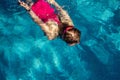 Above top view of little cute kid girl in sport pink swimsuit and goggles diving underwater in clear blue water of Royalty Free Stock Photo
