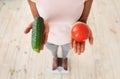 Above view of African American lady holding tomato and cucumber, standing on scales, choosing healthy diet, closeup Royalty Free Stock Photo