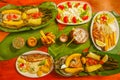 Above view of assorted food, grilled meat with potato, sweet tomatos, salad, pepper, fried plantain, fish in a leaf with Royalty Free Stock Photo