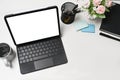 Computer tablet, flower pot, coffee cup and book on white office desk.