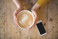 Above view of female hands holding hot cup of coffee and with smart phone with on wooden table. Royalty Free Stock Photo