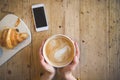 Above view of female hands holding hot cup of coffee and with smart phone with on wooden table. Coffee break at work. Royalty Free Stock Photo