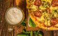 Above view of foam of tasty beer in a glass close to a delicious pizza with salami and herbs served on wooden table Royalty Free Stock Photo