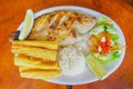 Above view of fried fish served with side salad, rice, and yucca served in a white plate over a wooden table Royalty Free Stock Photo