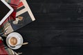 Above view of newspaper, scarf in a cage, tablet and cup of latte coffee on black wooden background. Royalty Free Stock Photo