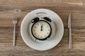Vintage alarm clock in white porcelain plate on wooden table with cutlery set Royalty Free Stock Photo