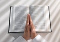 Above view of woman holding hands clasped while praying over Bible at white table Royalty Free Stock Photo