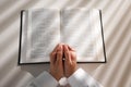 Above view of woman holding hands clasped while praying over Bible at white table Royalty Free Stock Photo