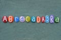 Abracadabra, magic word composed with multi colored stone letters over green sand