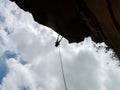 Abseiling a negative sanstone rock wall with blue sky on background - view from bellow Royalty Free Stock Photo