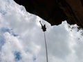 Abseiling a negative sanstone rock wall with blue sky on background - view from bellow