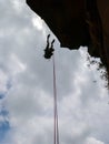 Abseiling a negative sanstone rock wall with blue sky on background - view from bellow