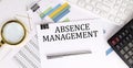 ABSENCE MANAGEMENT text on the white paper on the light background with charts paper ,keyboard and calculator