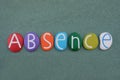 Absence word composed with multicolored stone letters over green sand