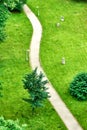 Abstract aerial view of winding footpath running along trees and bushes through manicured lawn area