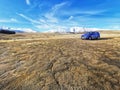 An abstract background image of a brown dry winterly ground with snow covered mountain range on the background and small blue car